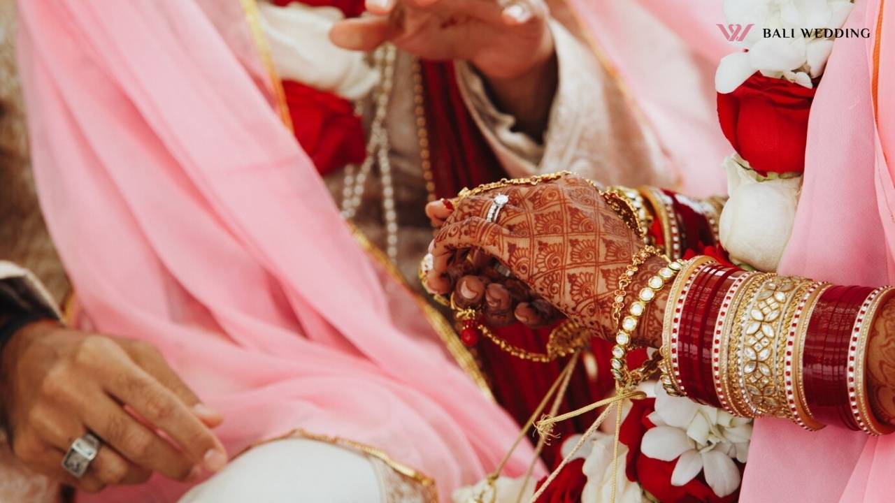 Close-up of the bride and groom holding hands during an Indian wedding ceremony, highlighting the intricate henna designs and traditional bridal bangles.
