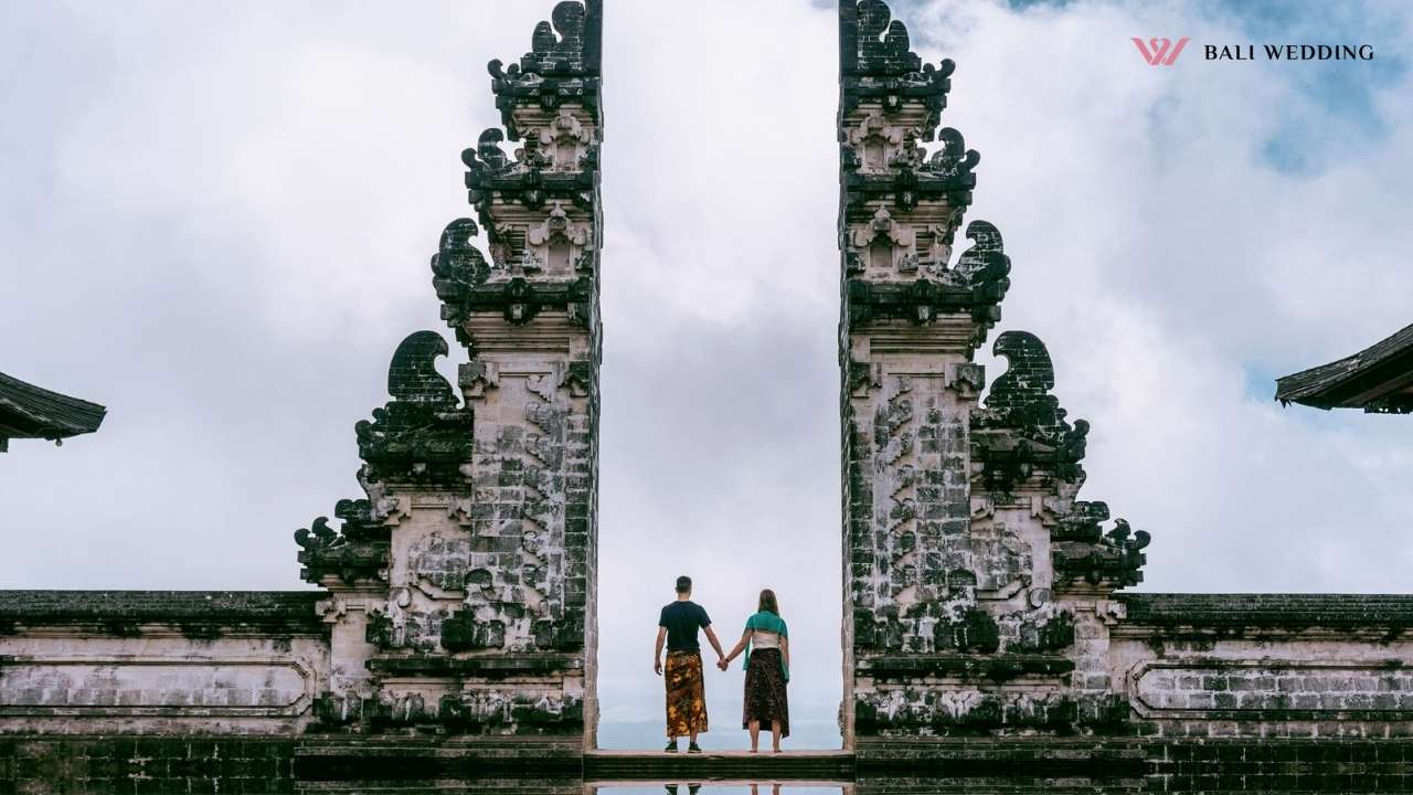 Couple holding hands between Balinese temple gates.