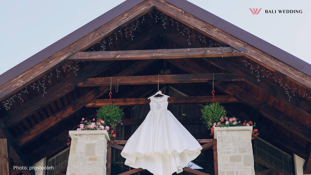 rustic-wedding-dress-hanging Wedding dress hanging elegantly on a rustic wooden beam at a wedding venue.