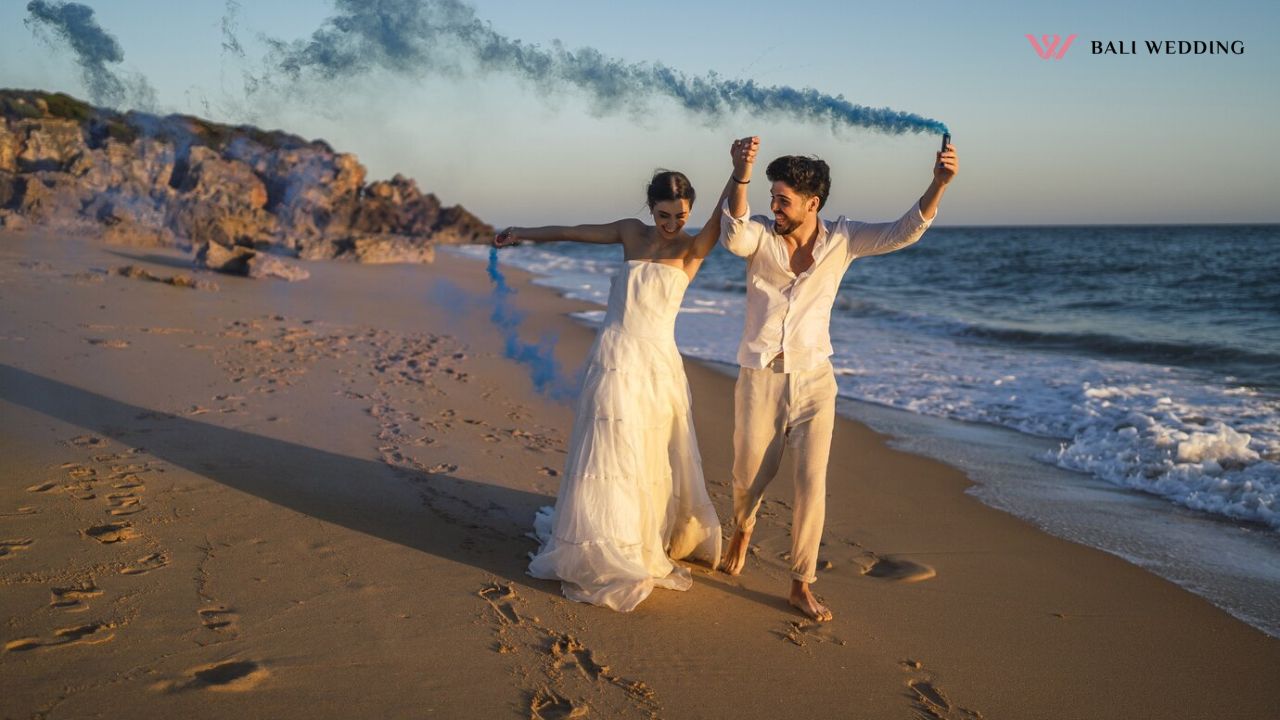 Picture of a beautiful couple posing with a blue smoke bomb in the beach Picture of a beautiful couple posing with a blue smoke bomb in the beach
