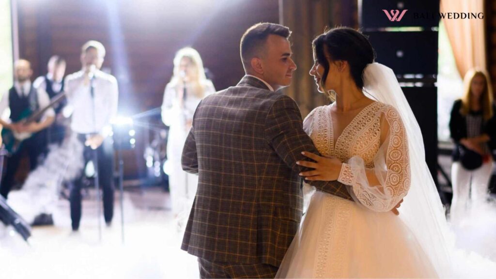 Front view of beautiful bride in amazing wedding dress with long sleeves holding groom hands and looking to him during first wedding dance